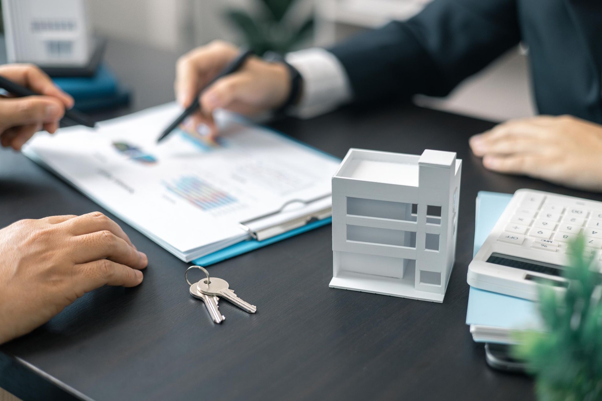 Two people are sitting at a table with a model house and keys.