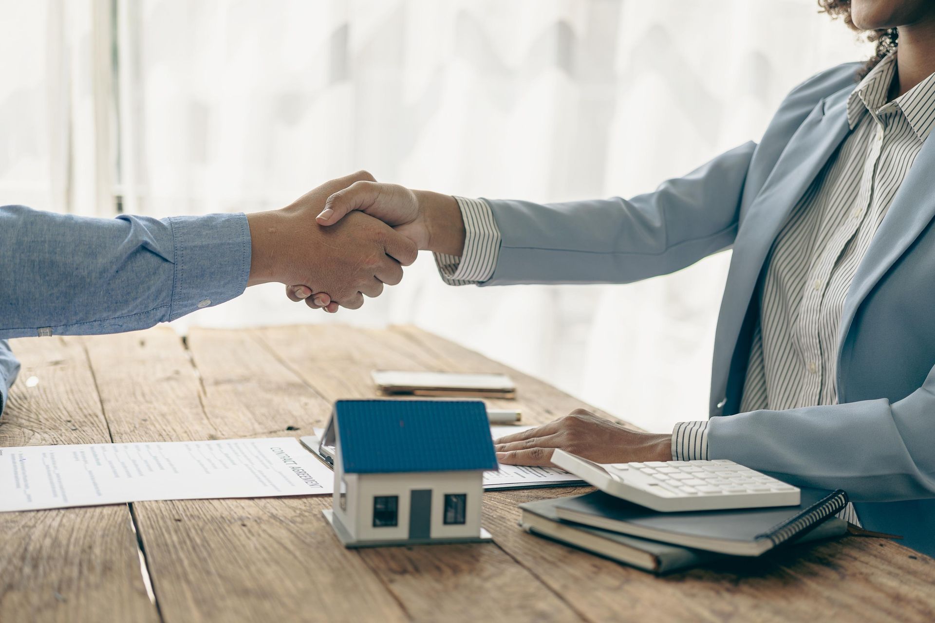 A man and a woman are shaking hands over a table with a model house on it.