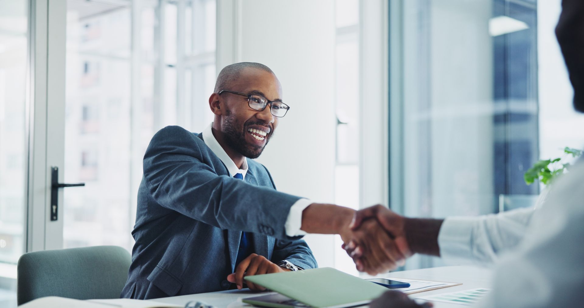 A man is shaking hands with another man while sitting at a table.