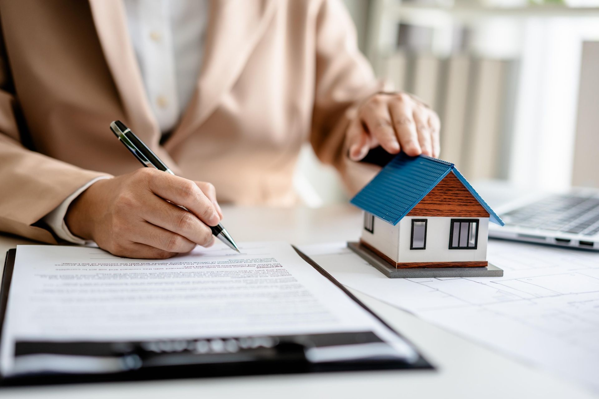 A woman is signing a document next to a model house.