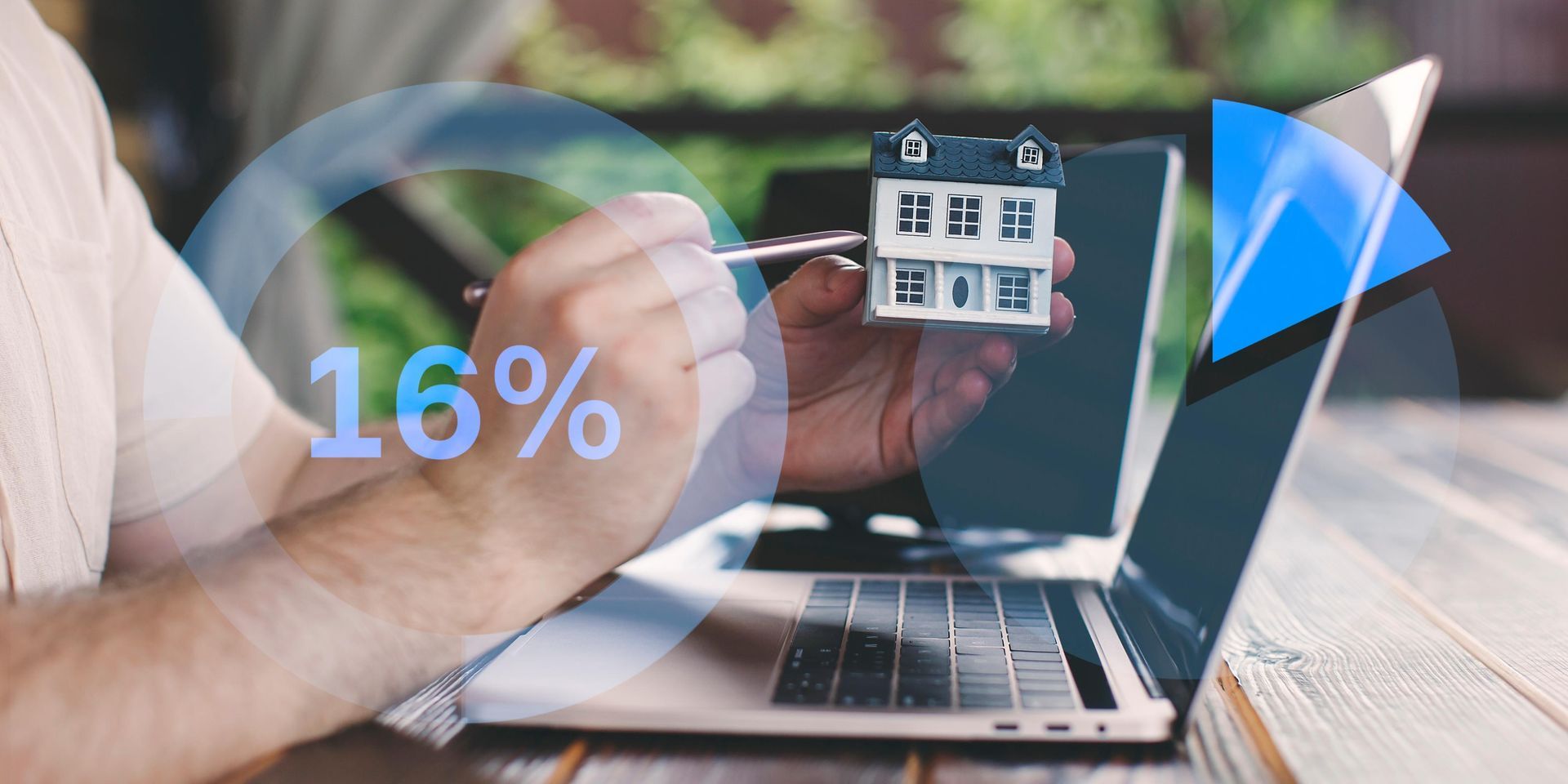 A man is holding a small house in front of a laptop computer.