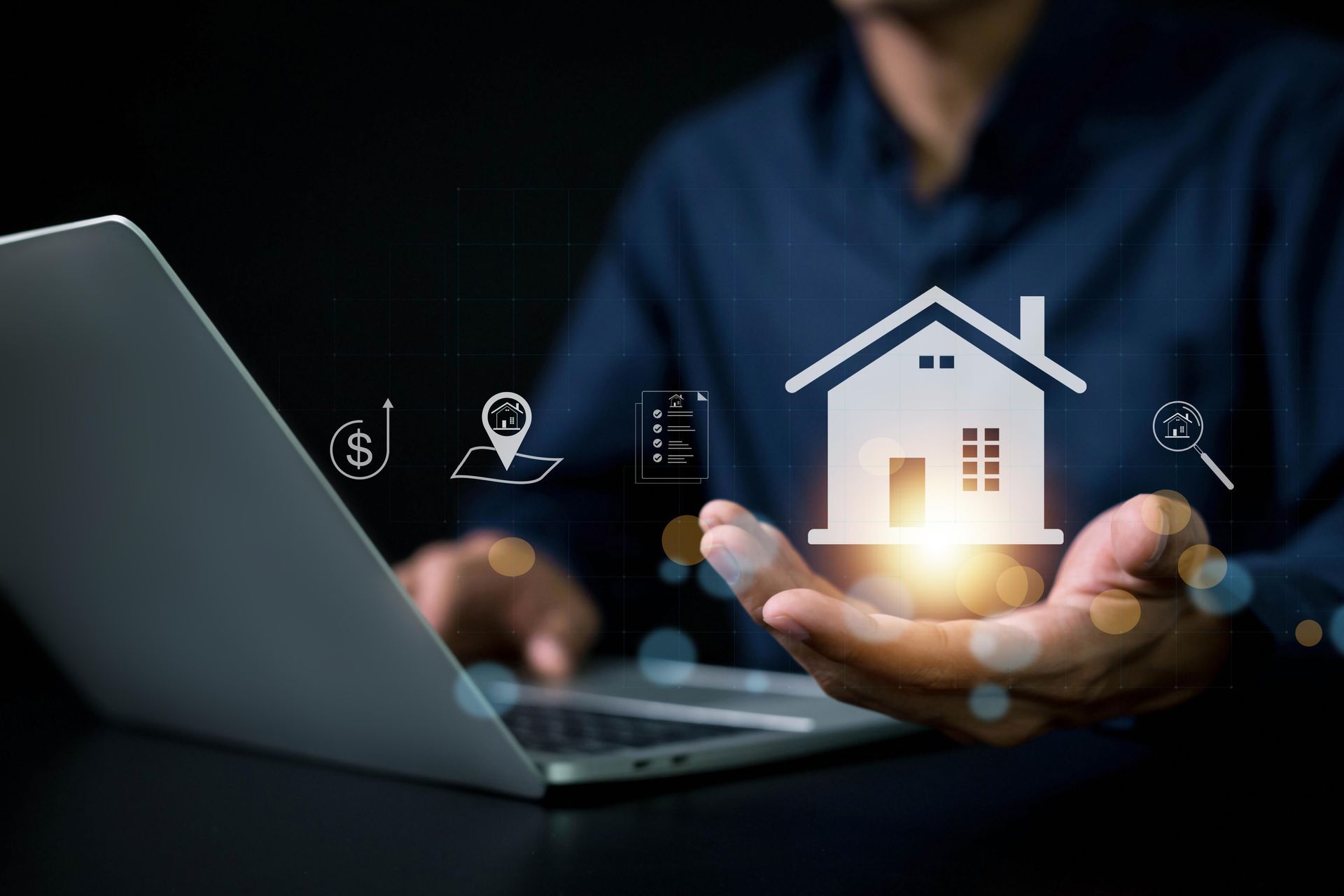 A man is holding a house in front of a laptop computer.