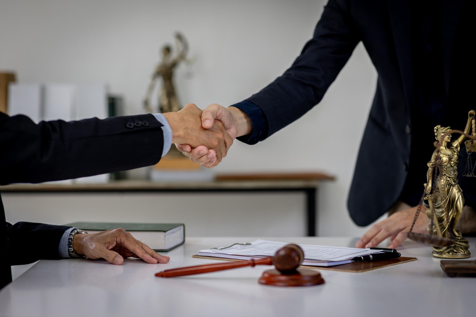 Two men are shaking hands over a table with a statue of justice in the background.