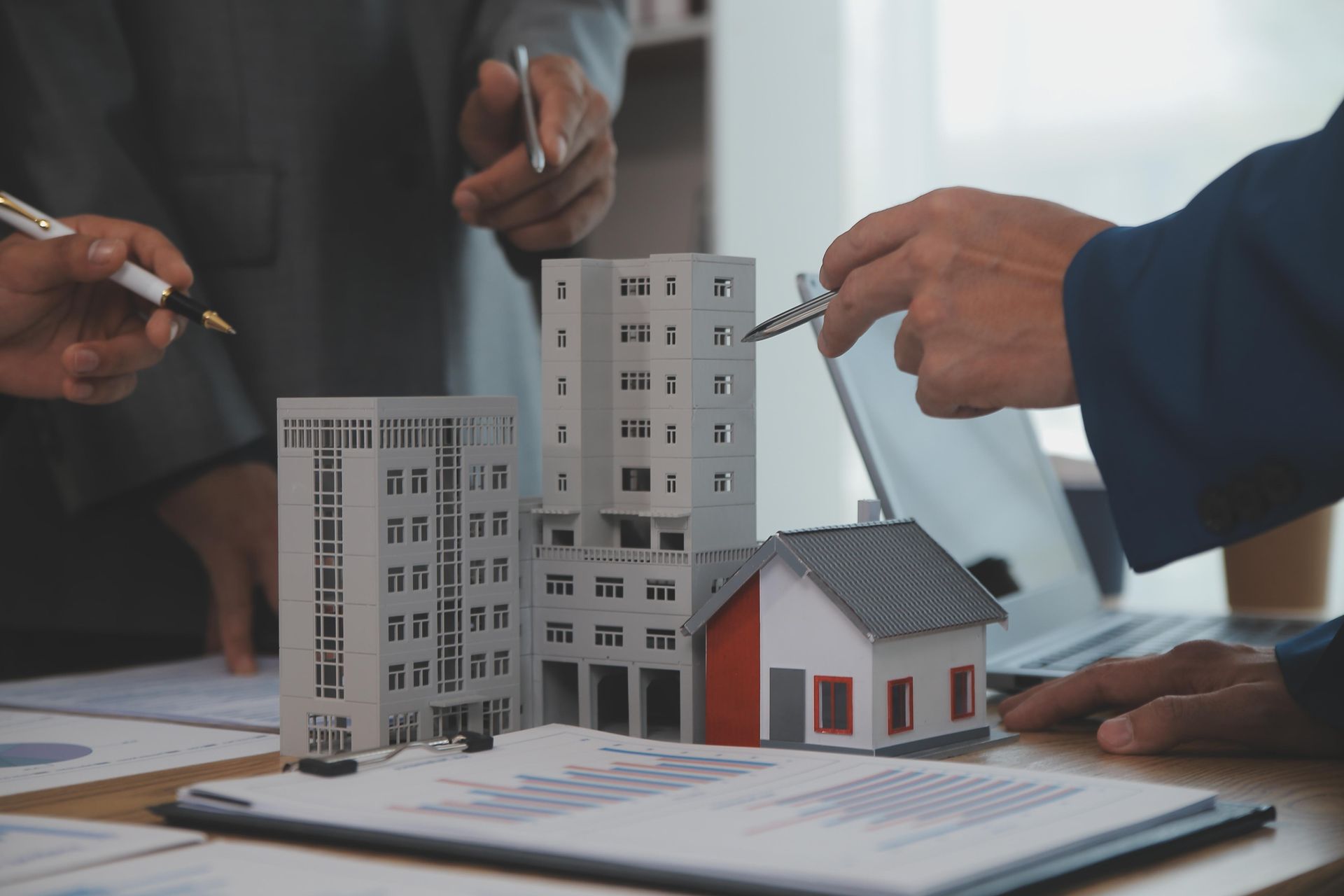 A group of people are sitting at a table looking at a model of a building and a house.