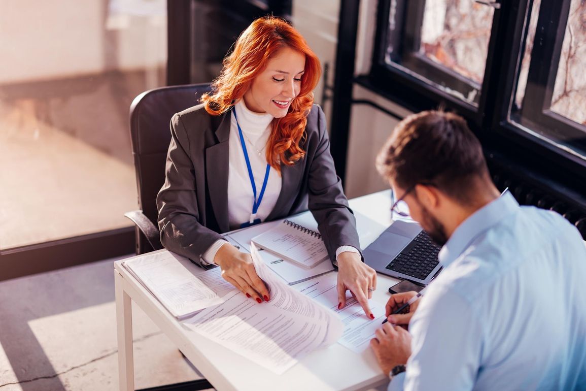 A woman is sitting at a desk talking to a man.