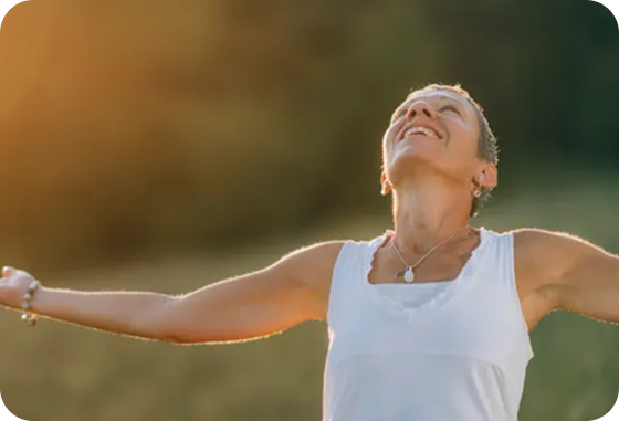 A woman in a white tank top is standing in a field with her arms outstretched.