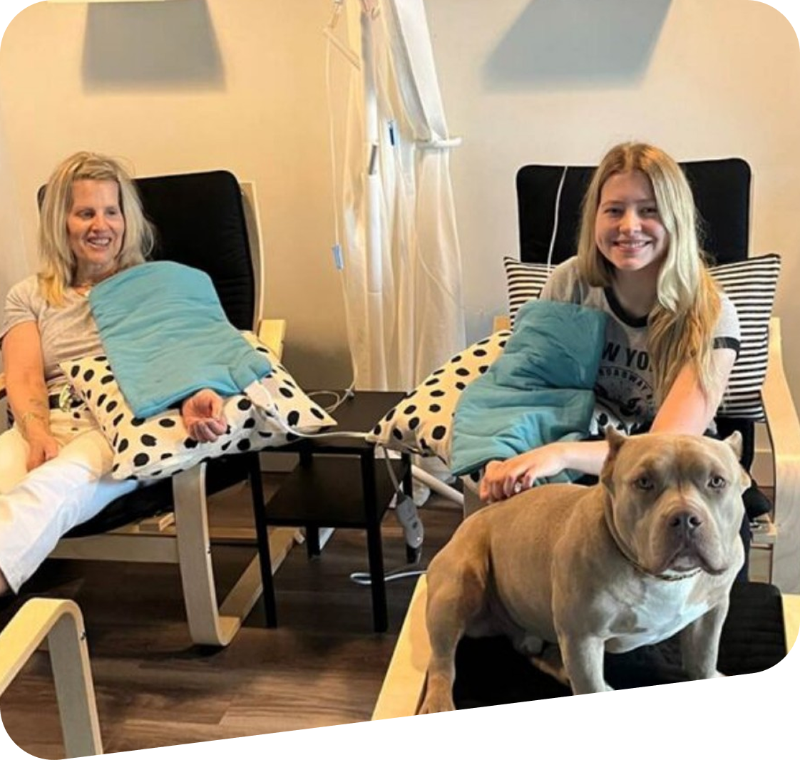 Two women are sitting in chairs next to a dog.