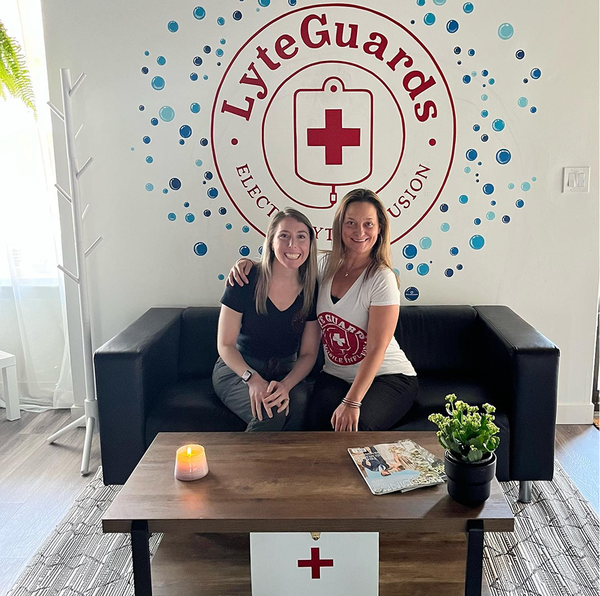Two women are sitting on a couch in front of a lyteguards logo
