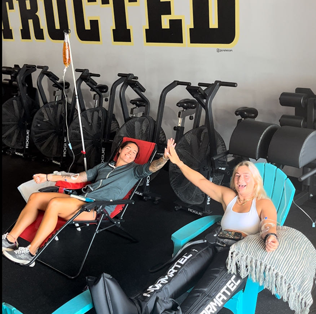 Two women are sitting in chairs in front of a sign that says