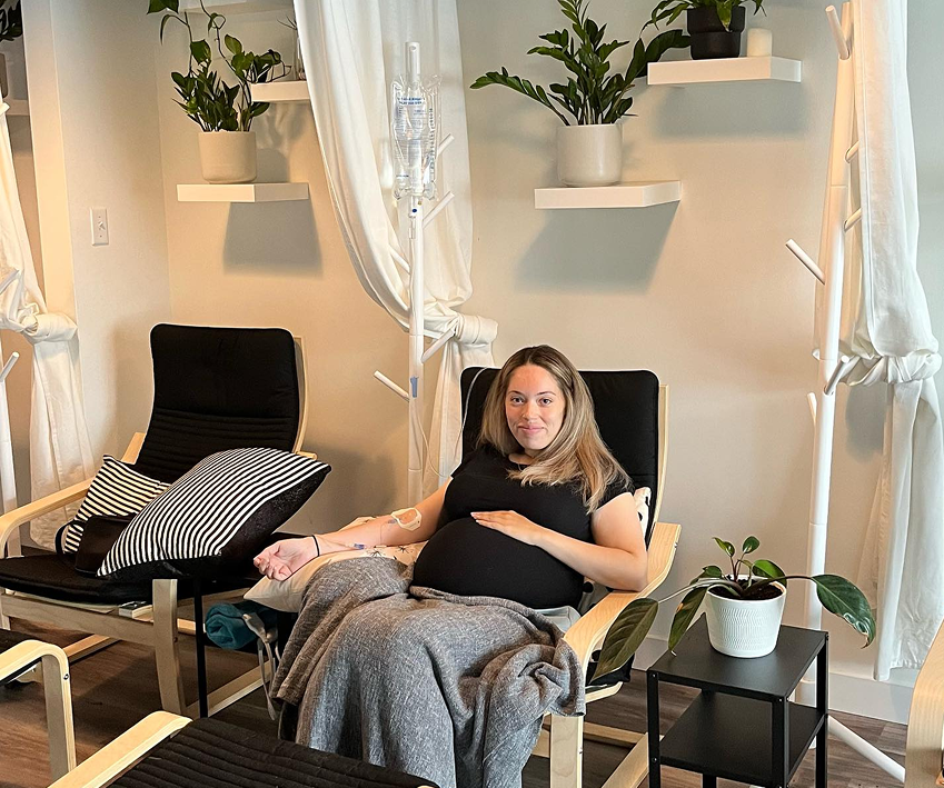 A pregnant woman is sitting in a chair with an iv in her arm.