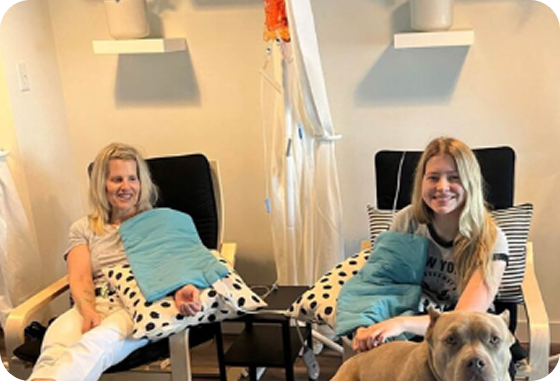 Two women are sitting in chairs next to a dog.