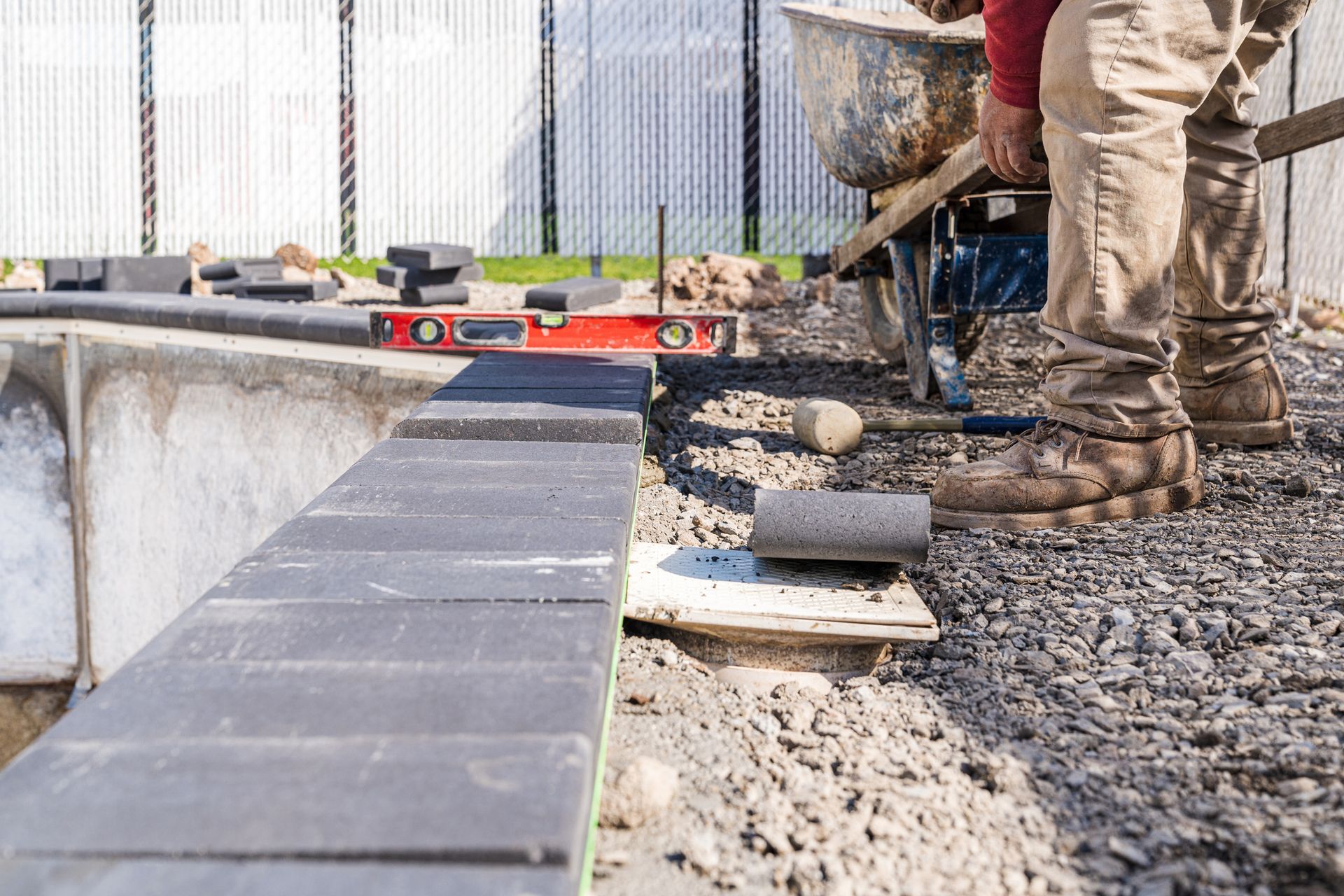 Worker laying bricks for a patio with tools and materials around.