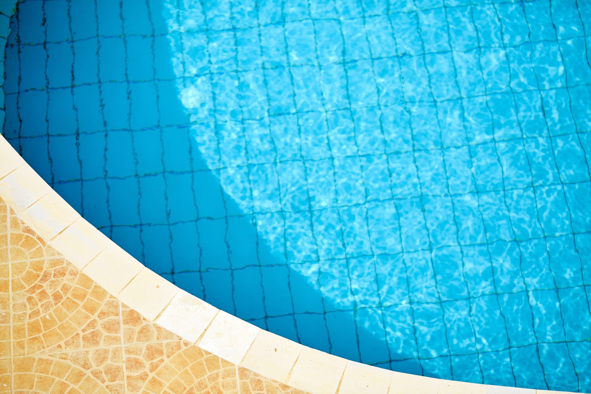 Close-up of the edge of a pool, paved with brick flooring. The pool has a blue shine and blue tiles.