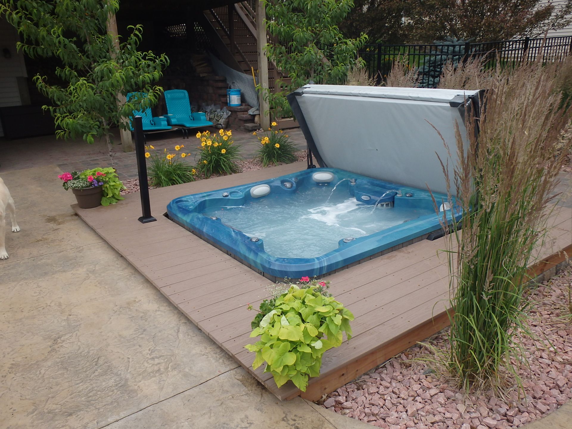 Hot tub on a wooden deck, partially covered. Landscaping includes flowers, plants, and decorative gravel. Hot tub on a wooden deck, partially covered. Landscaping includes flowers, plants, and decorative gravel.