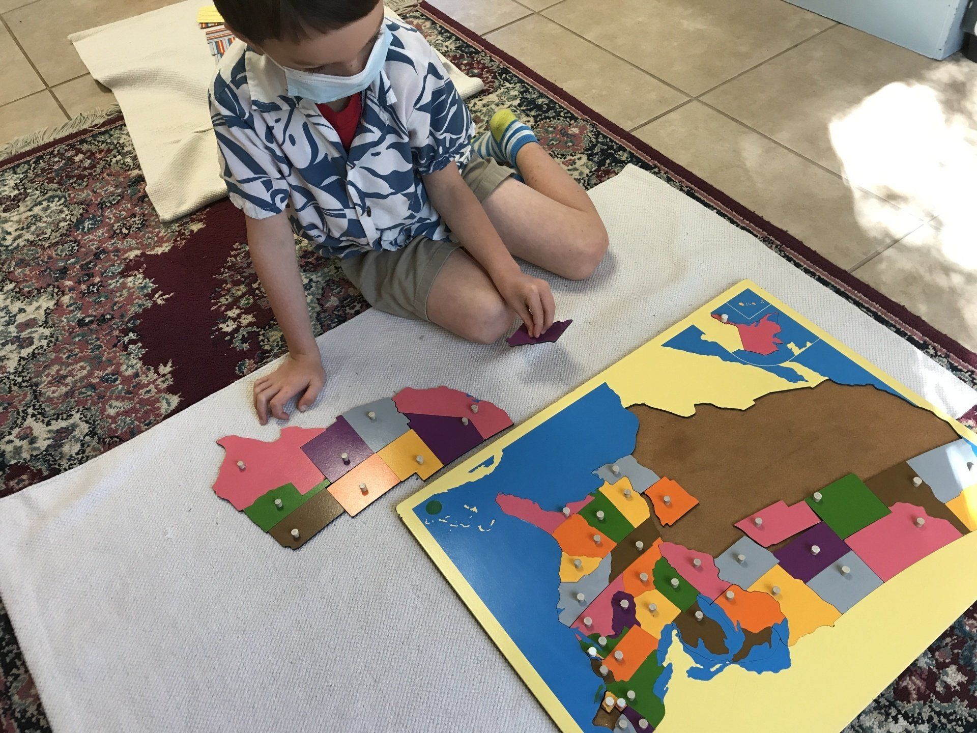A young boy wearing a mask is working with a montessori map puzzle