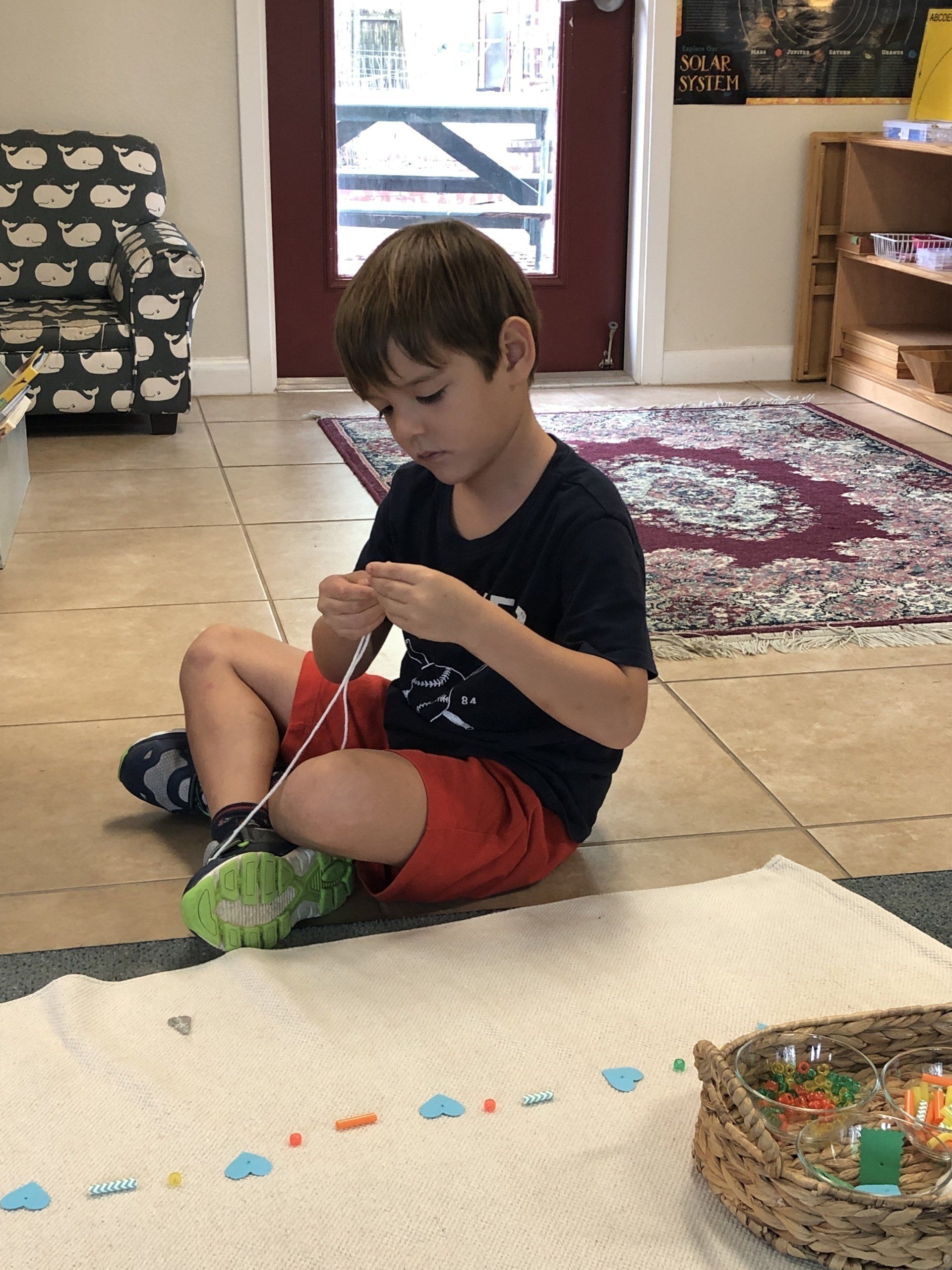 A young boy is sitting on the floor working montessori materials.