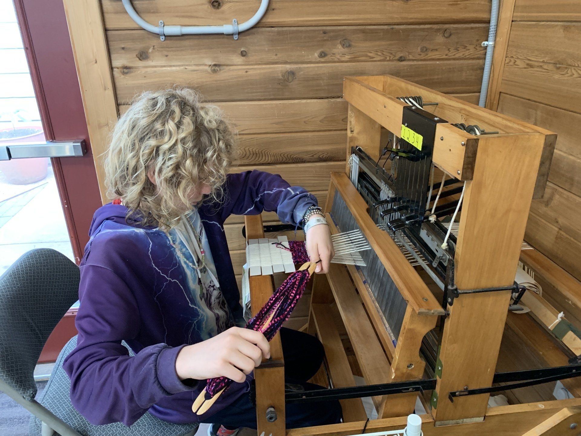 A woman is sitting in front of a wooden loom.