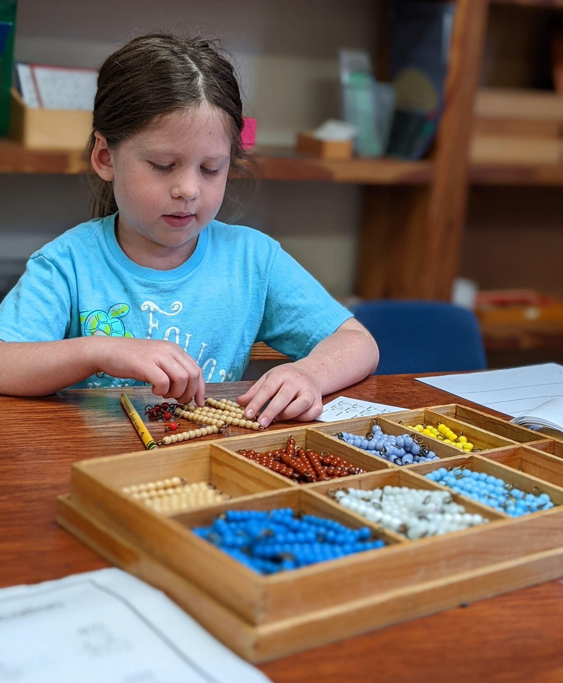 A little girl is sitting at a table playing with montessori math materials