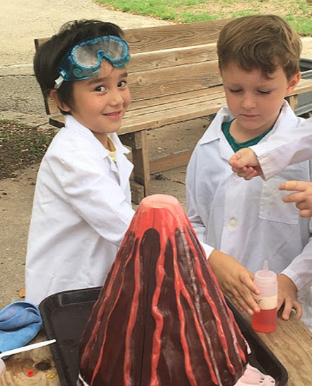 Two young boys are playing with a model volcano.