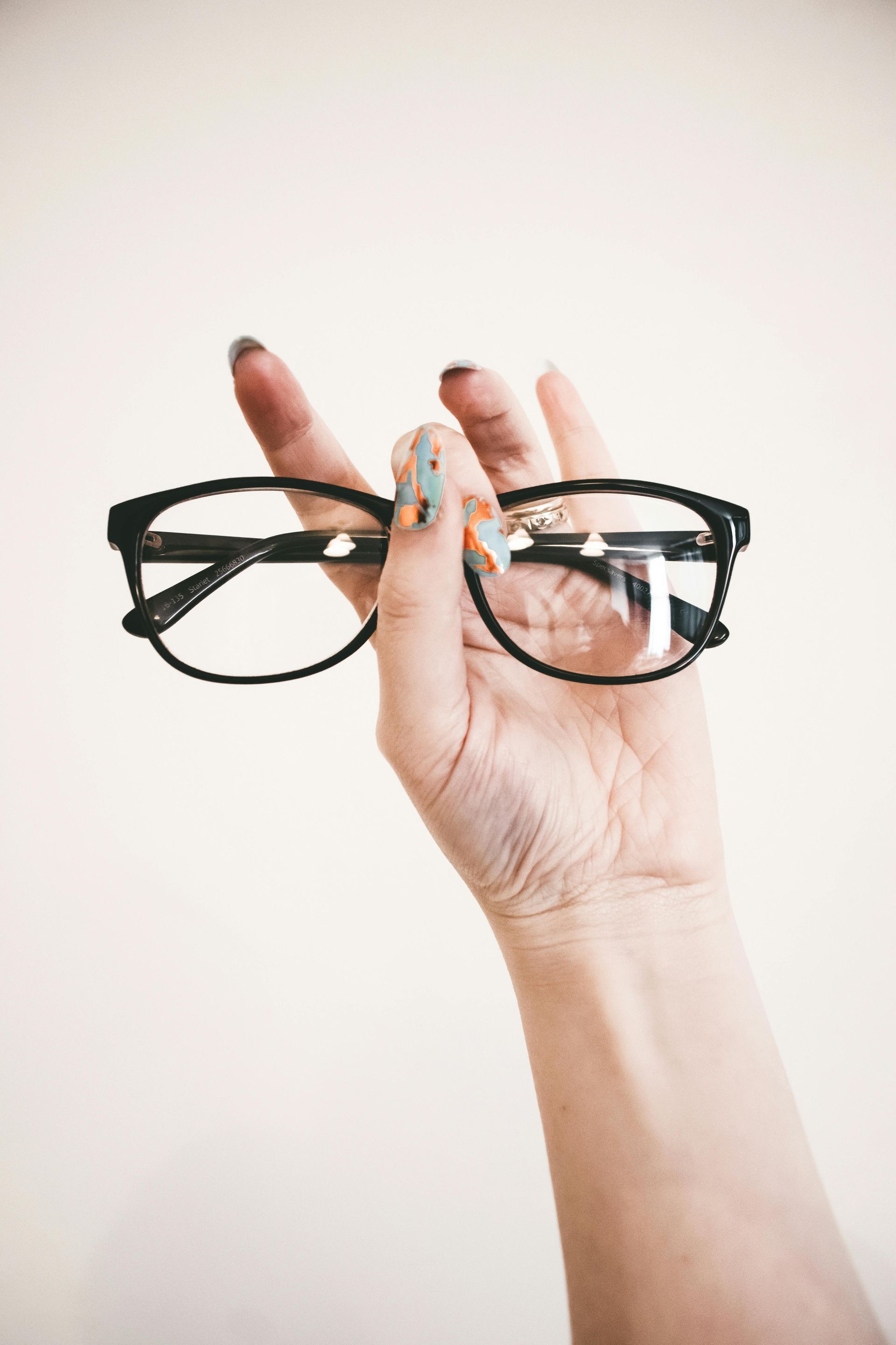 Hand holding black-framed eyeglasses against a white background.