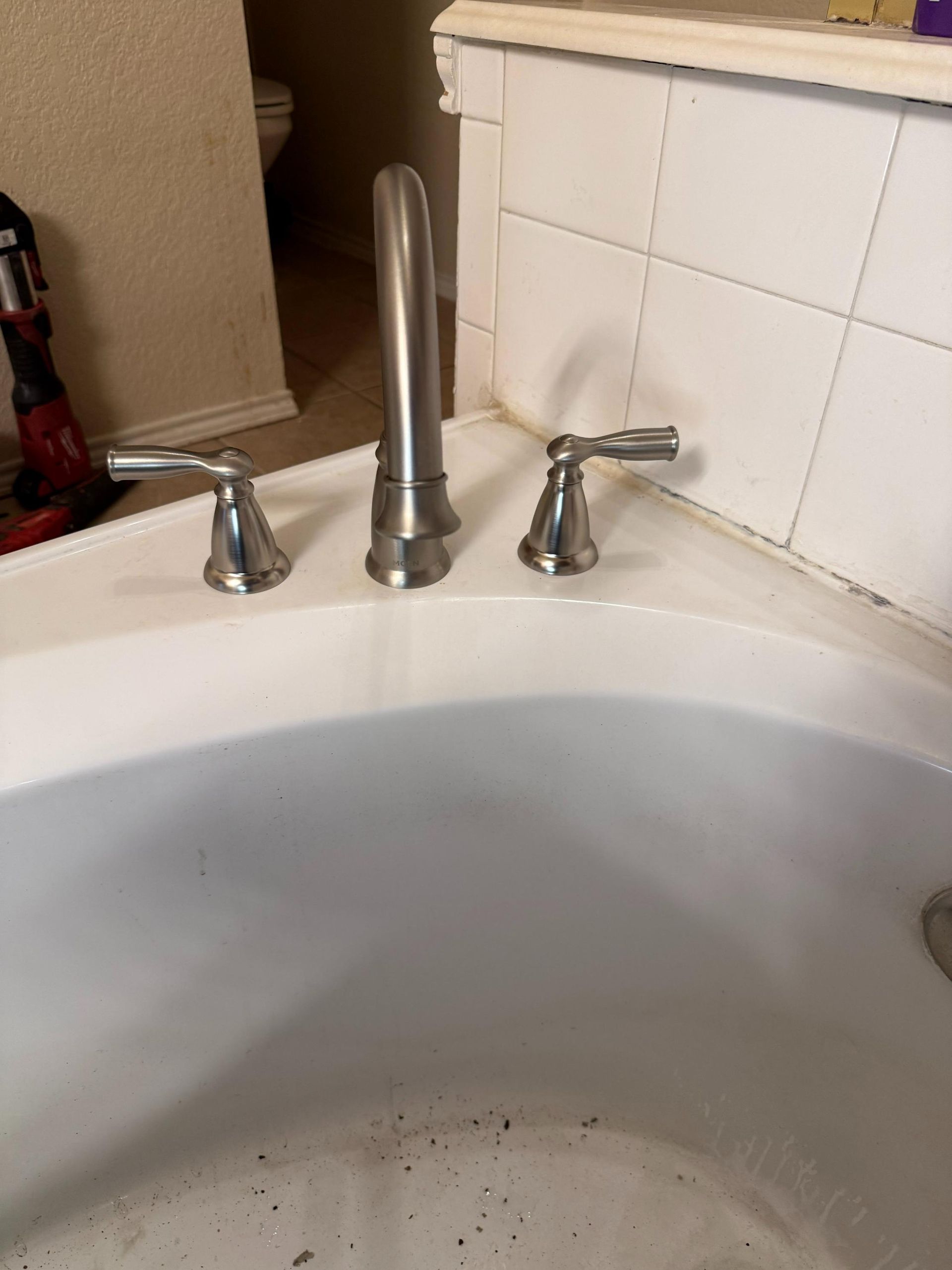 White bathtub with chrome faucet and handles. Tile wall in background.