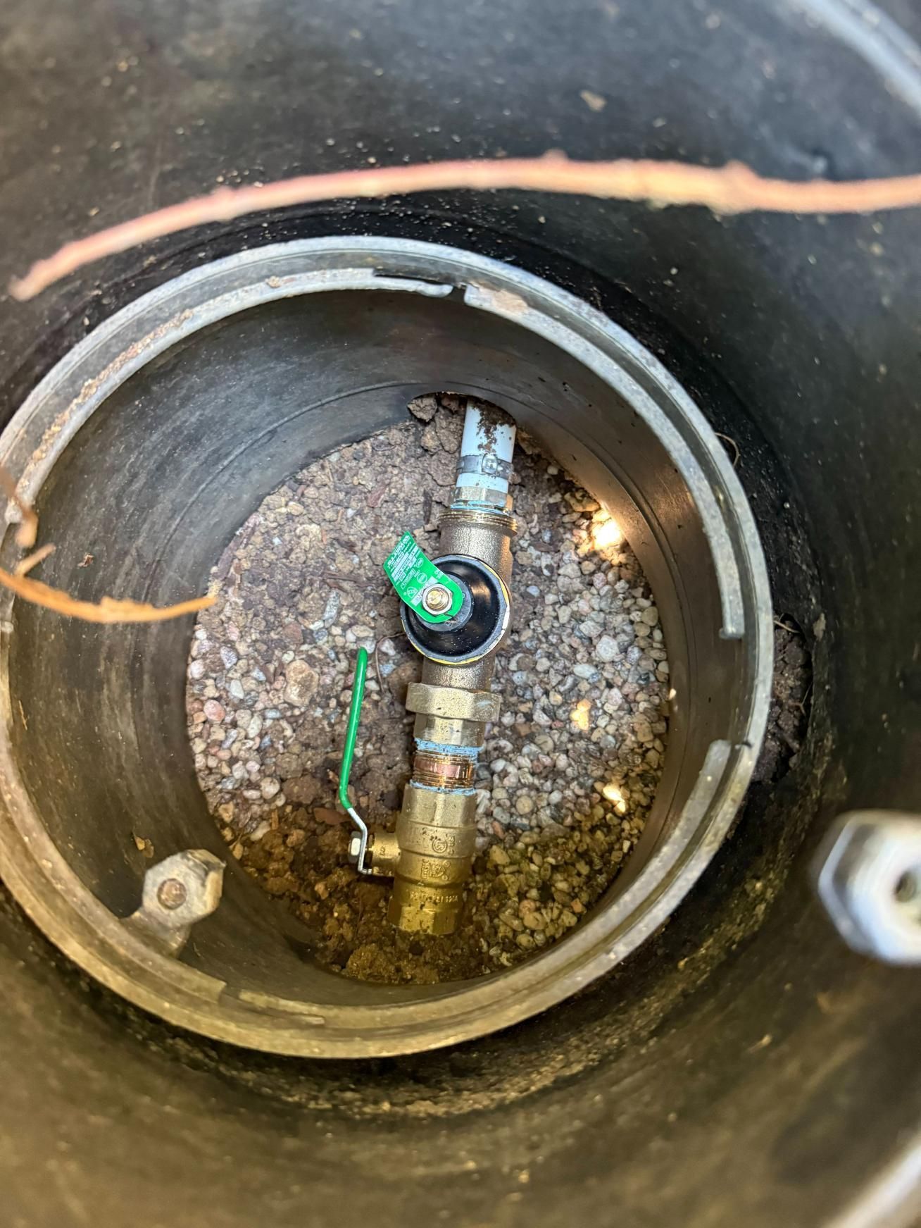 A water meter and shut-off valves inside a black plastic box filled with gravel.