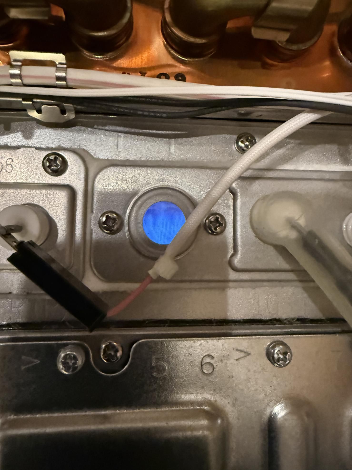 A blue flame burning in a small window, likely from a gas appliance. Wires and metal components are visible.