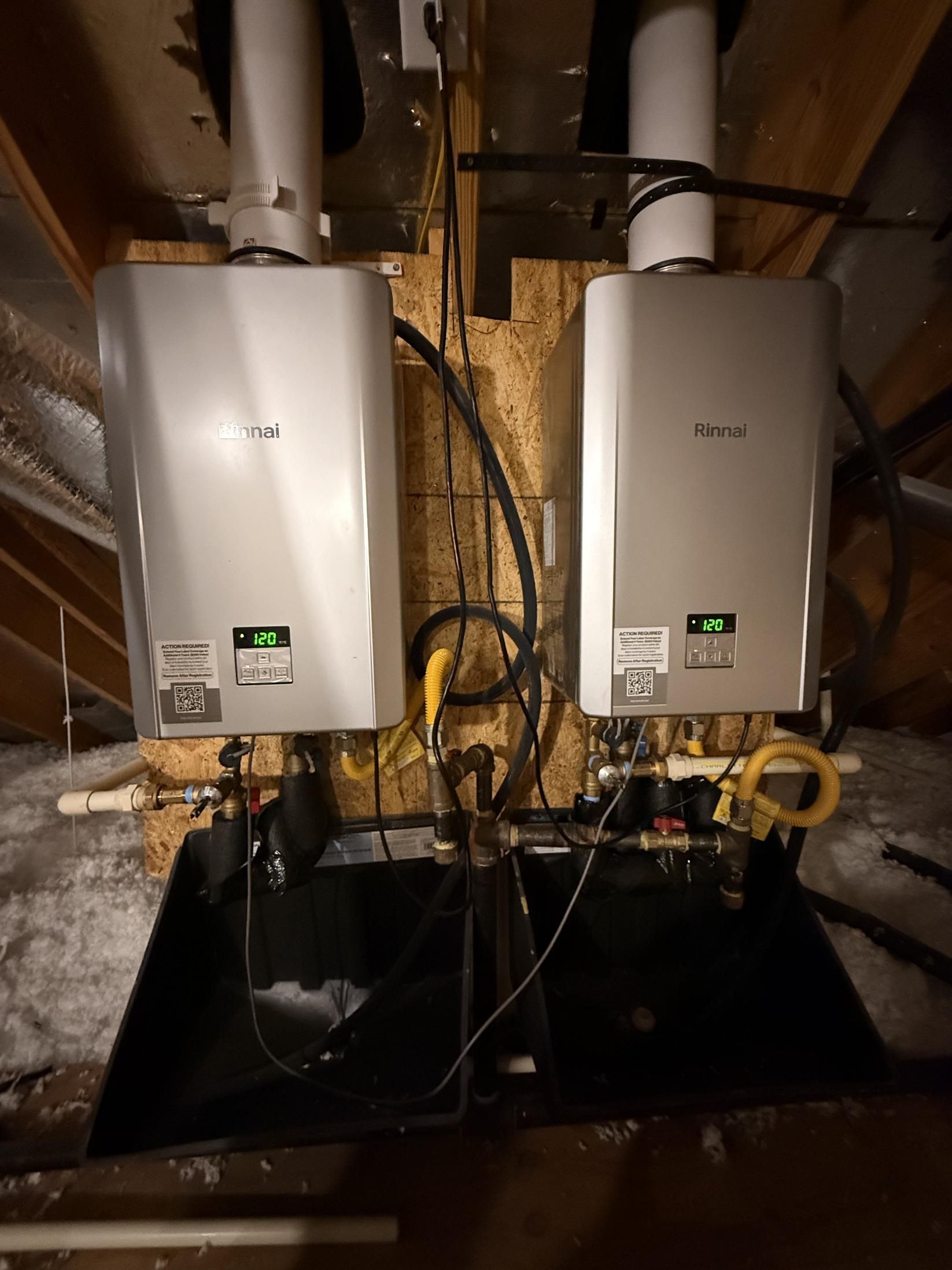 Two tankless water heaters mounted in an attic, with vent pipes and associated plumbing.