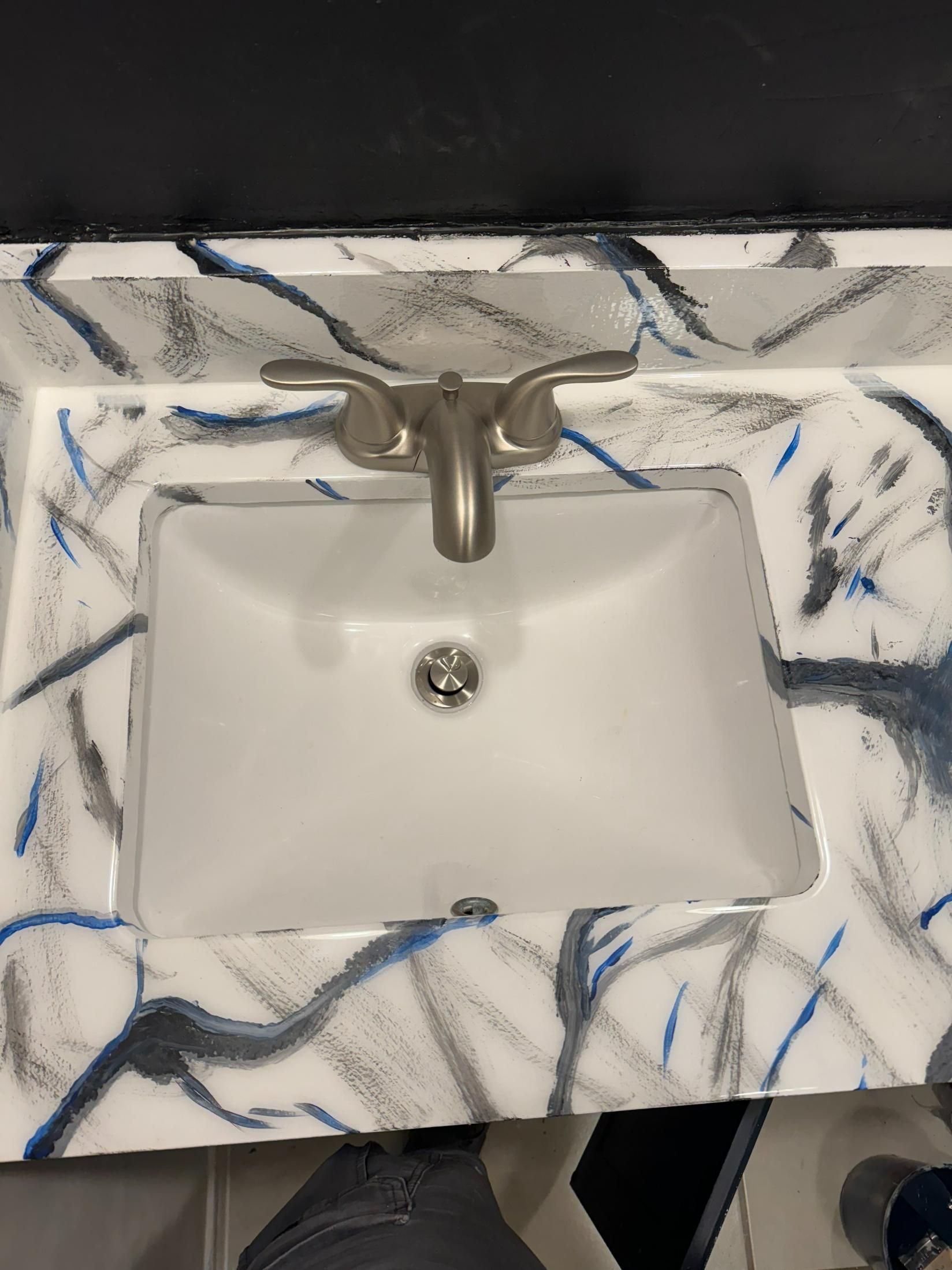White bathroom sink with silver faucet, on patterned countertop.