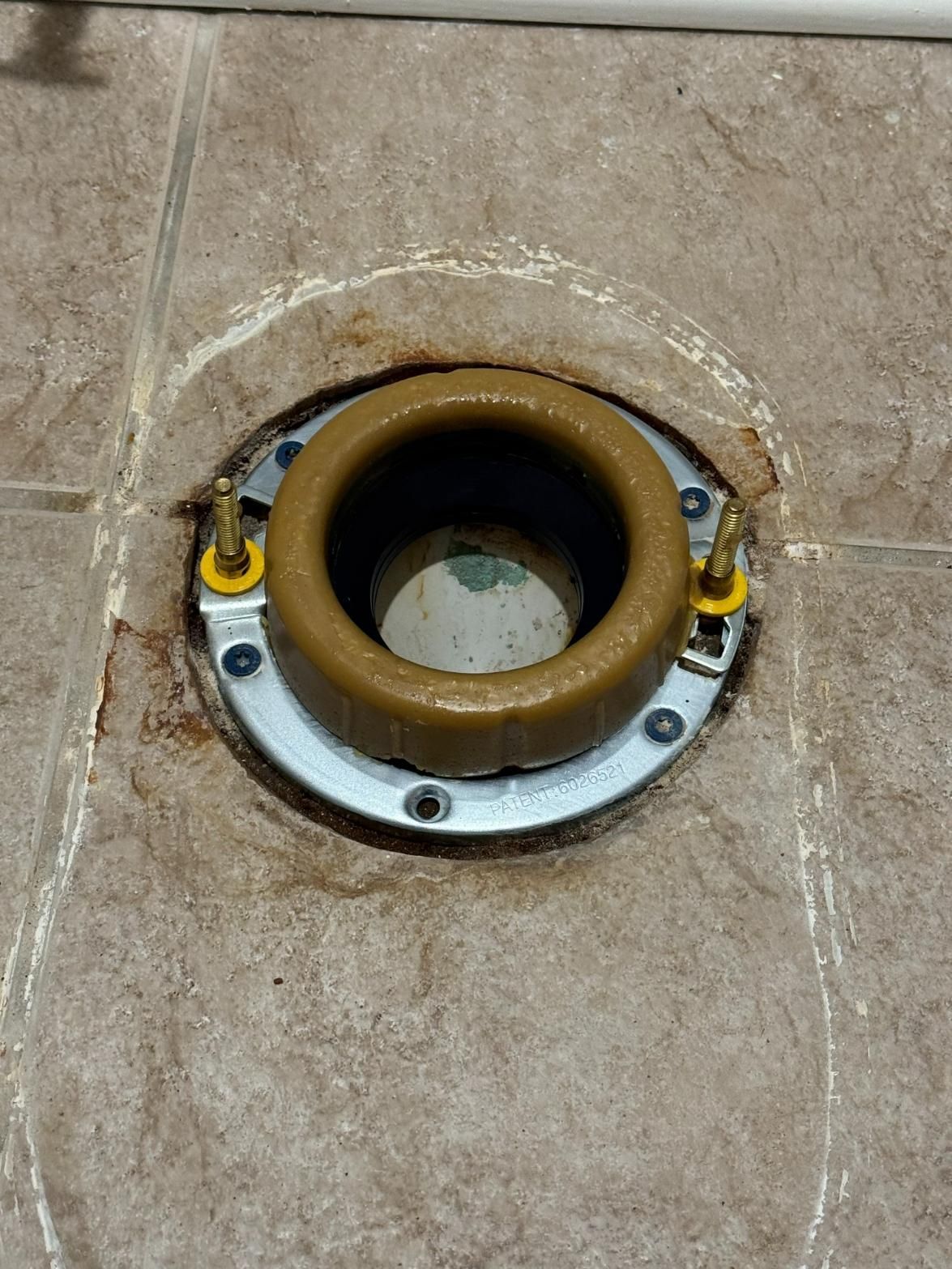 Toilet flange with wax ring installed on tiled floor, brass bolts are protruding.