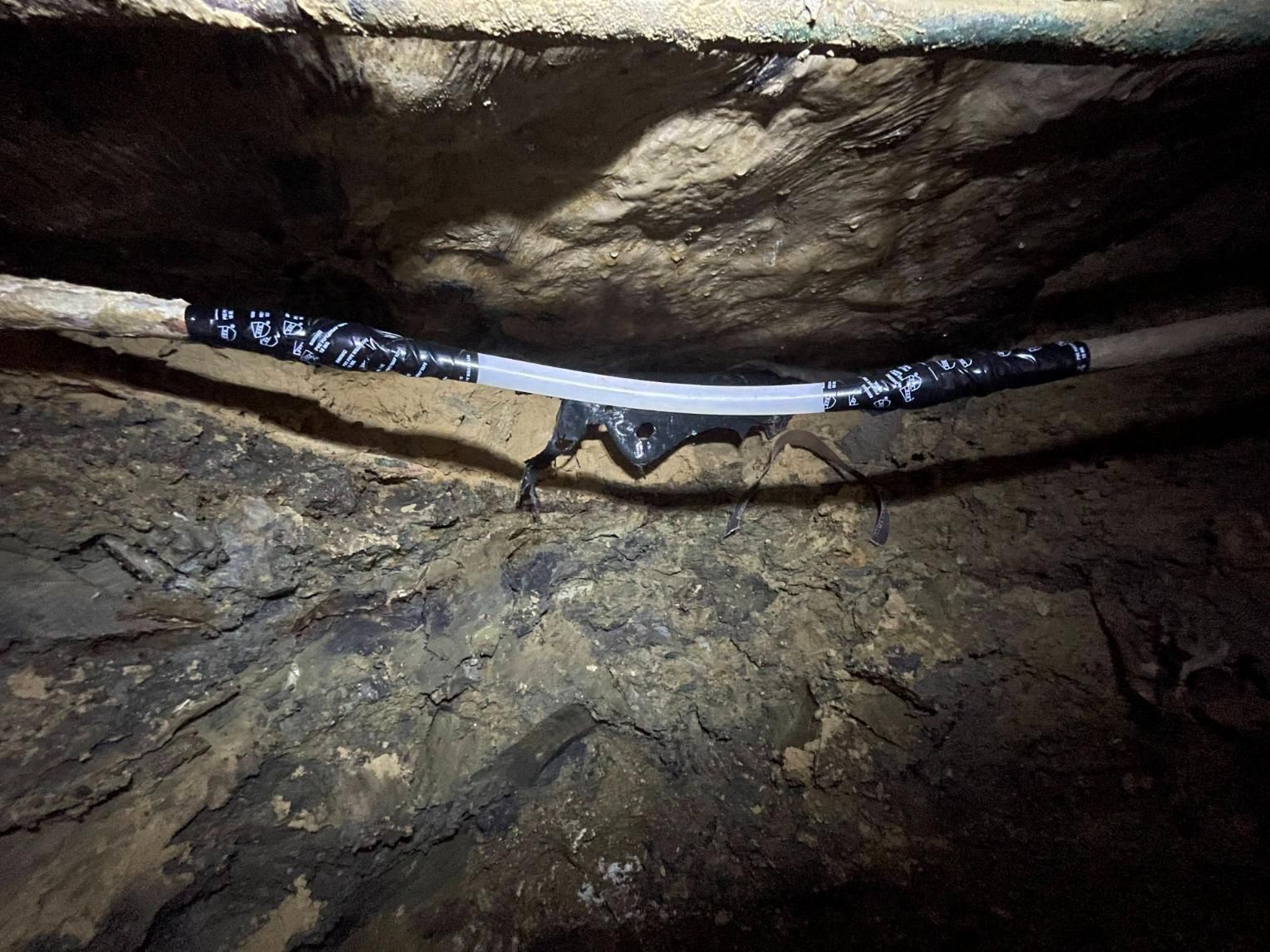 Pipe repair wrapped in black tape, leaking in a dark, rocky crevice.