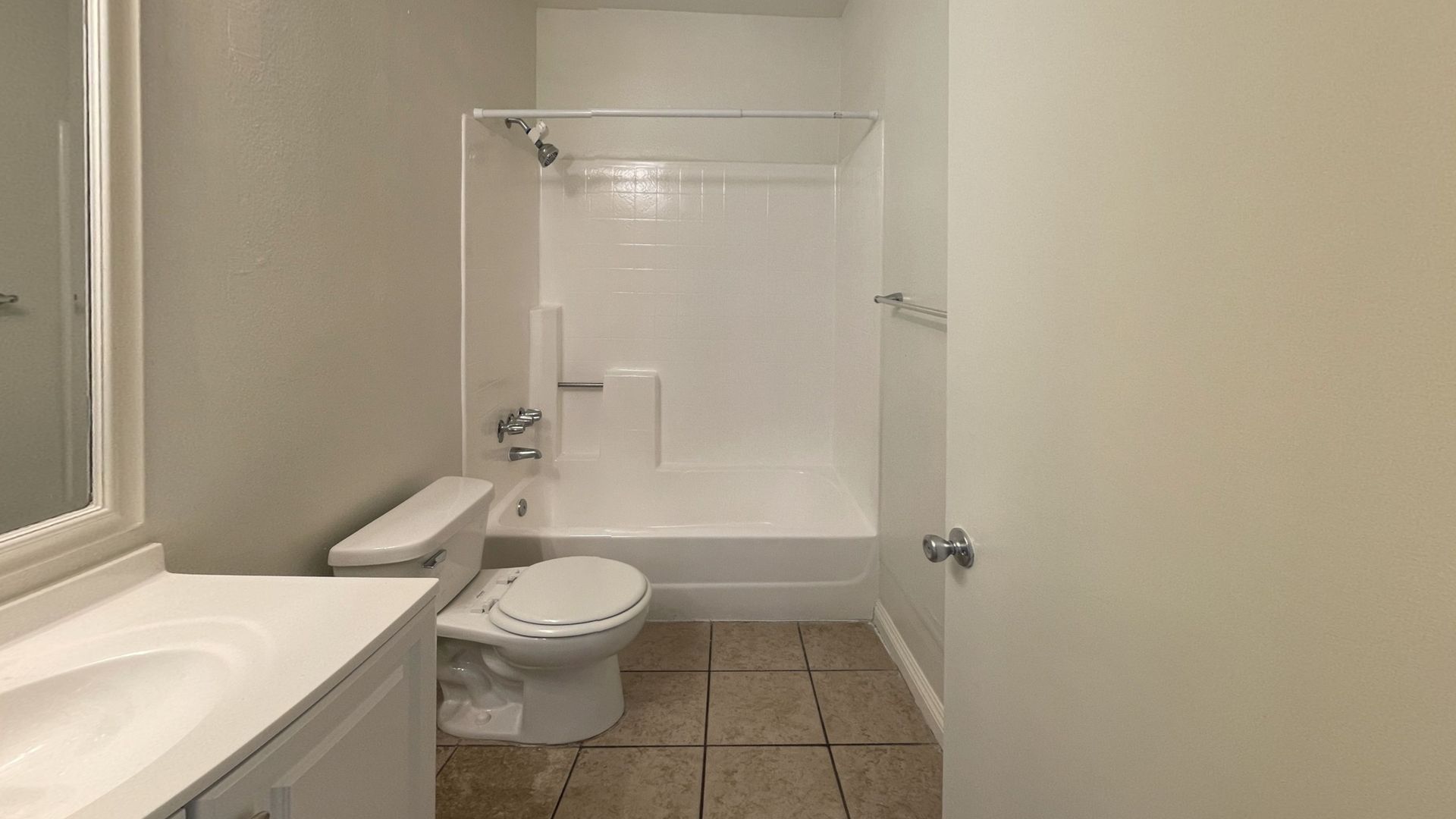Bathroom with white fixtures, shower, toilet, and sink. Beige tile floor and light gray walls.