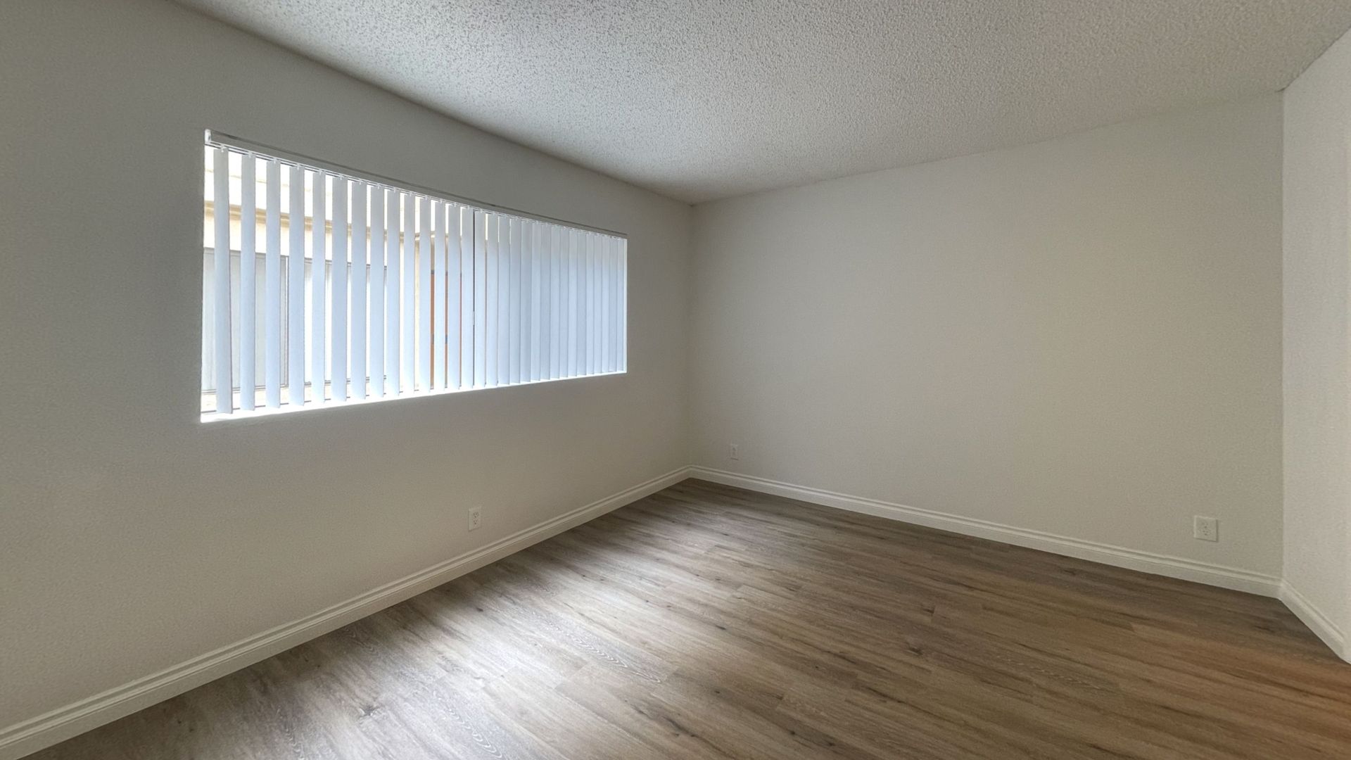 Empty room with a window, white walls, and wood-look flooring.