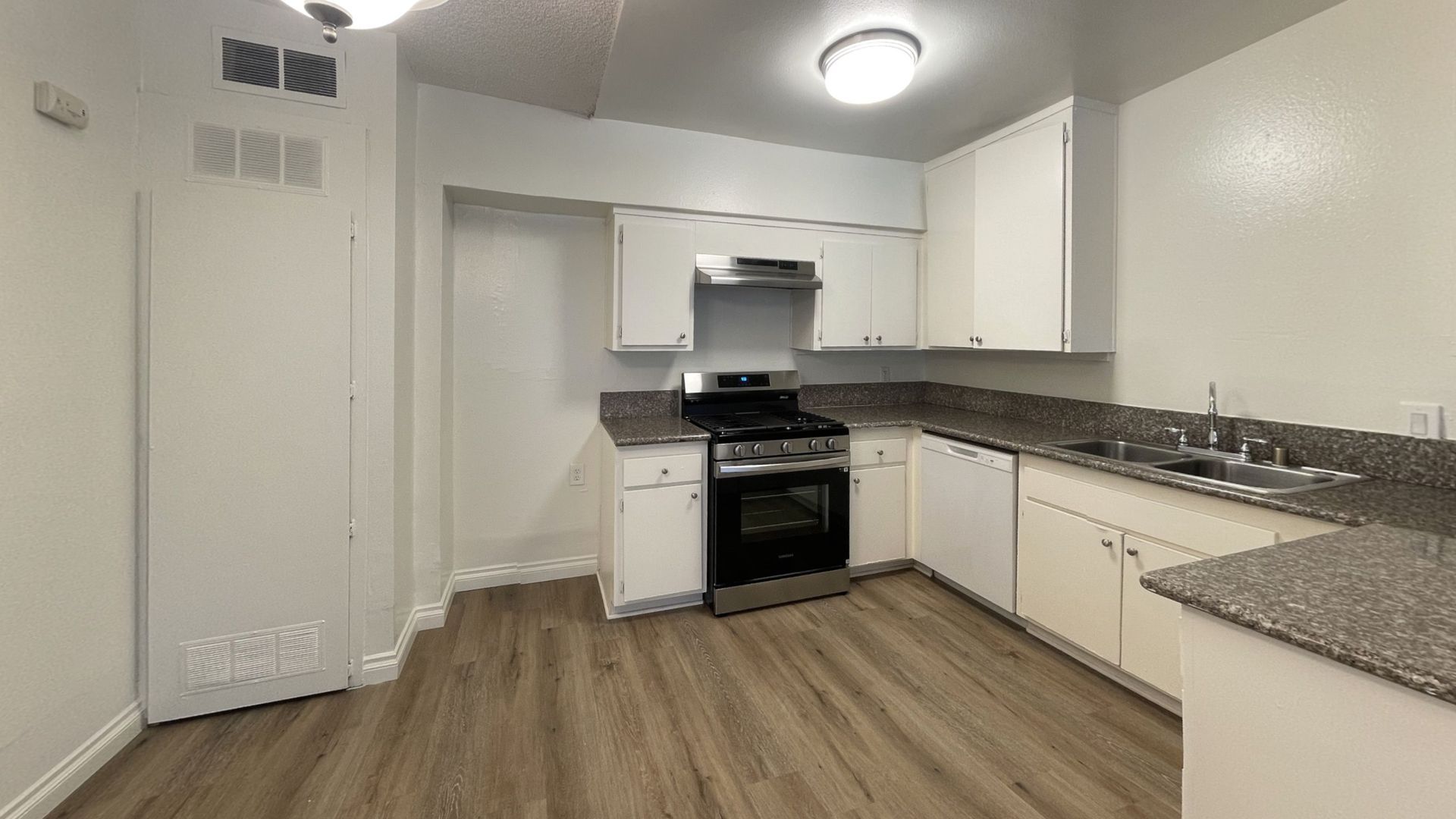 Kitchen with white cabinets, stainless steel appliances, and wood-look flooring.