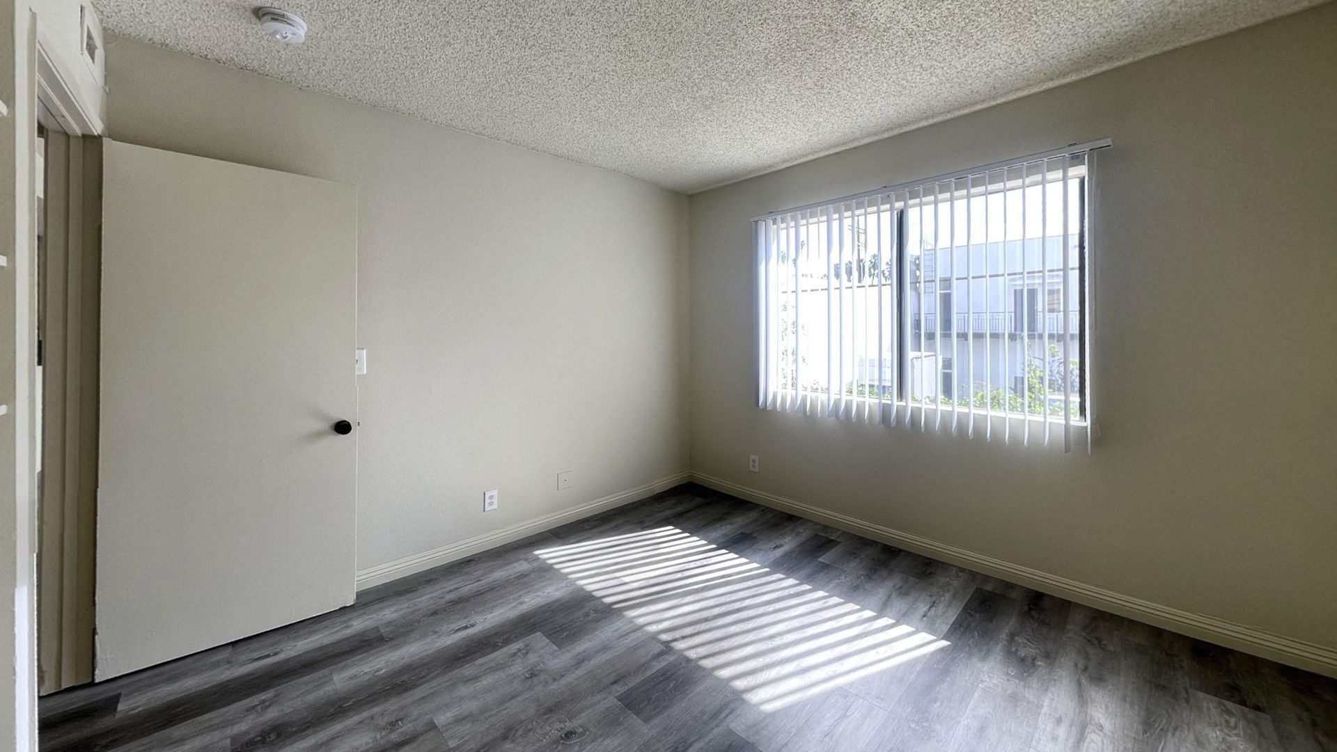 Empty room with gray wood-look flooring, light gray walls, and a window with blinds.
