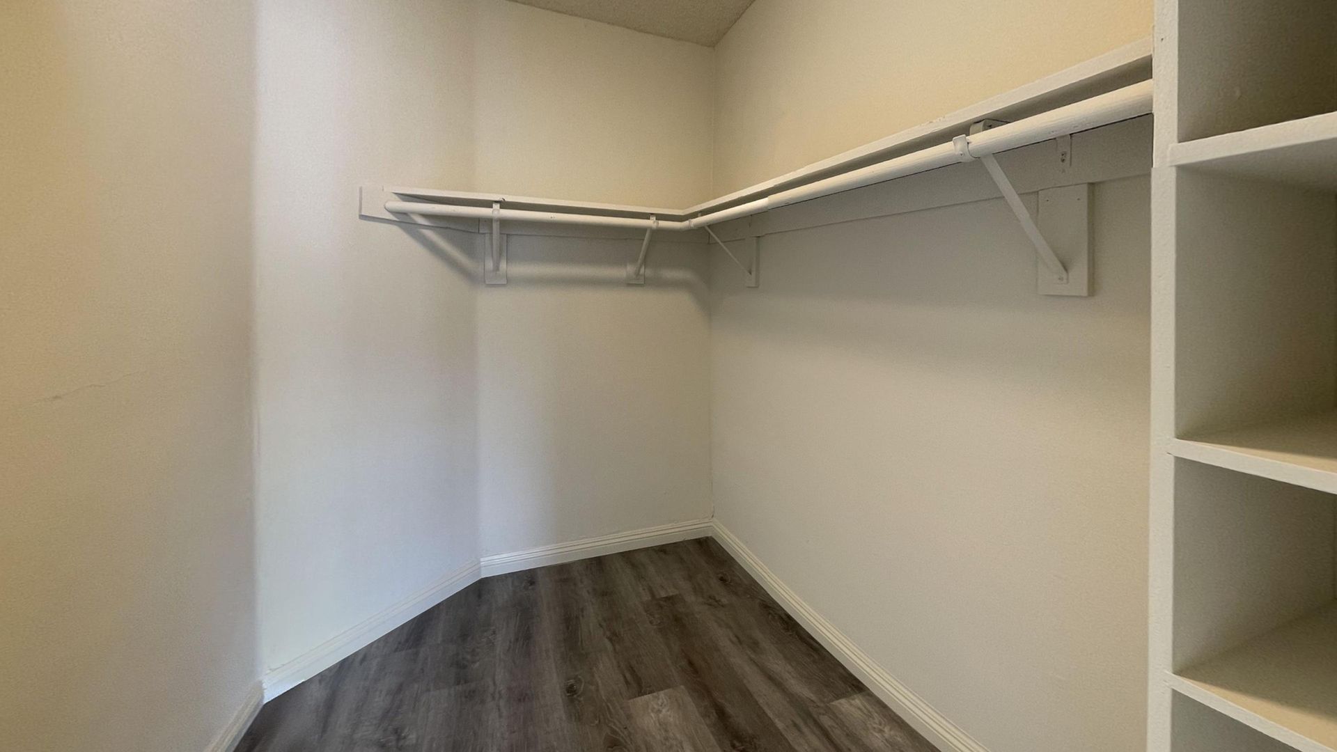 Empty walk-in closet with shelves and rod. White walls, grey flooring.