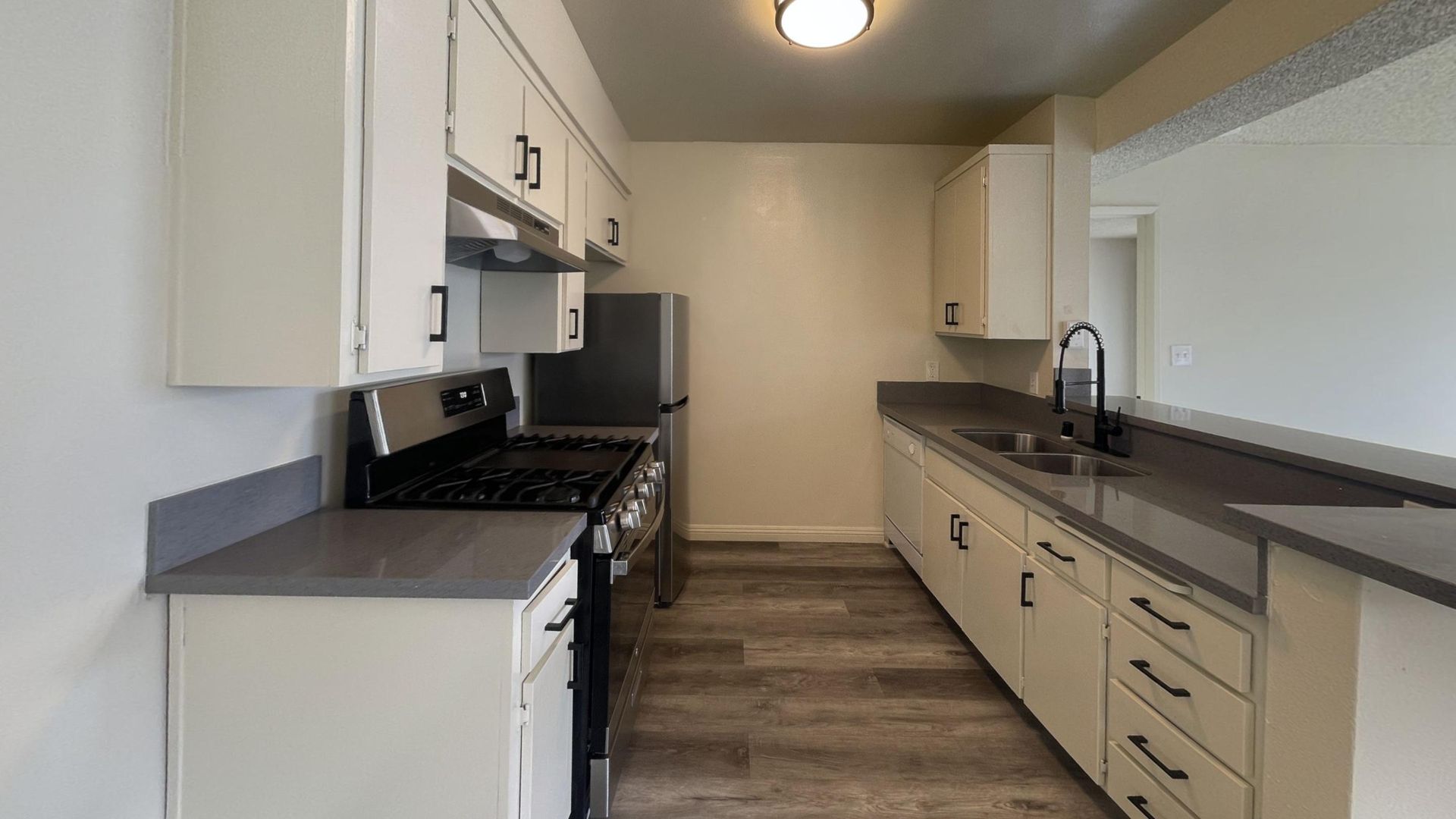 Kitchen with white cabinets, gray countertops, stainless steel appliances, and wood-look flooring.