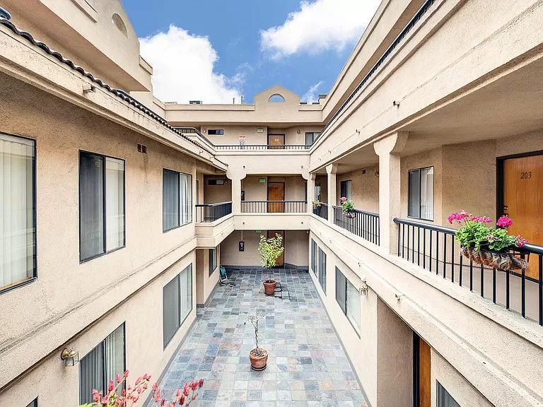 Courtyard of a beige apartment building with balconies, blue sky visible.