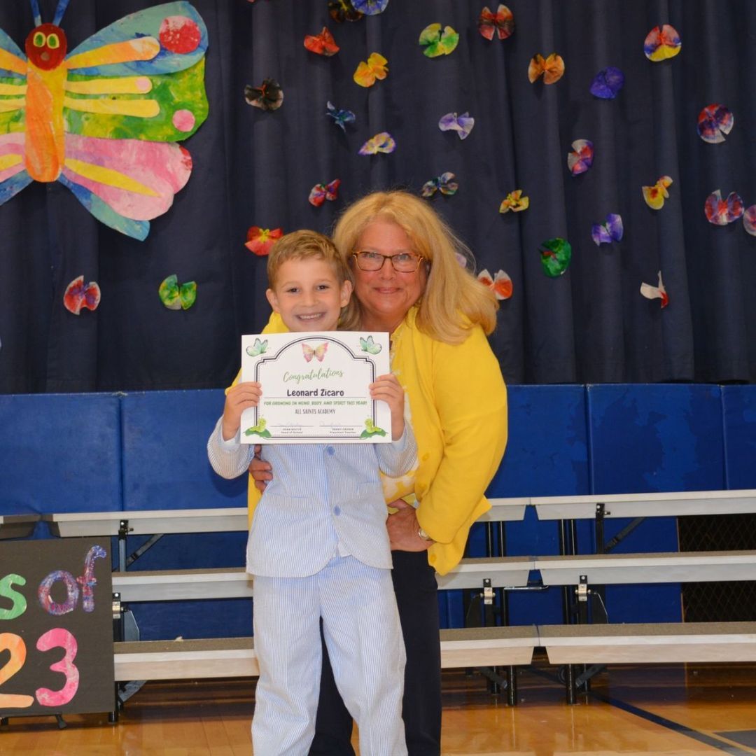 A woman holds a young boy who is holding a certificate