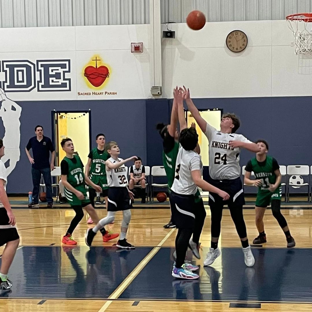 A group of boys are playing basketball in a gym with the word de on the wall