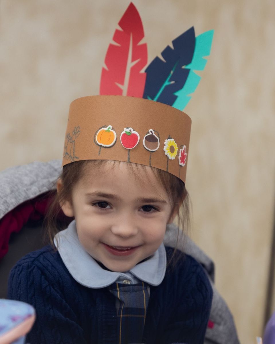 A little girl wearing a paper hat with feathers on it