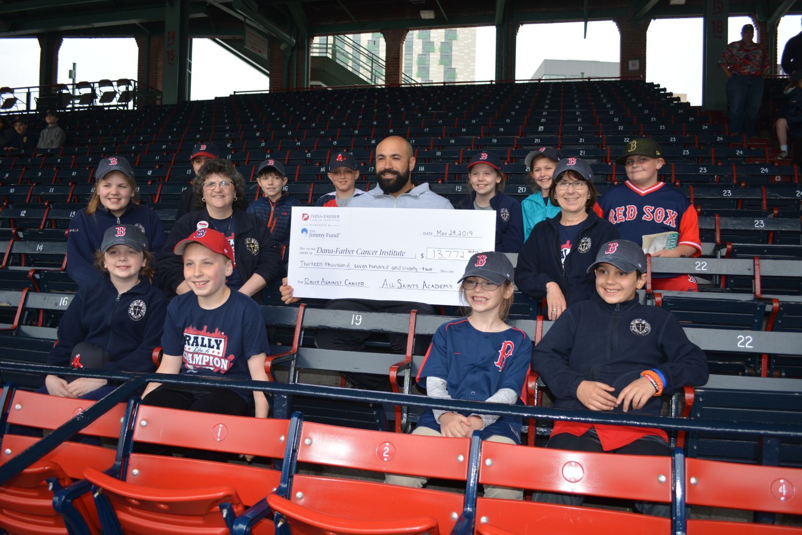 A group of kids sitting in a stadium holding a large check