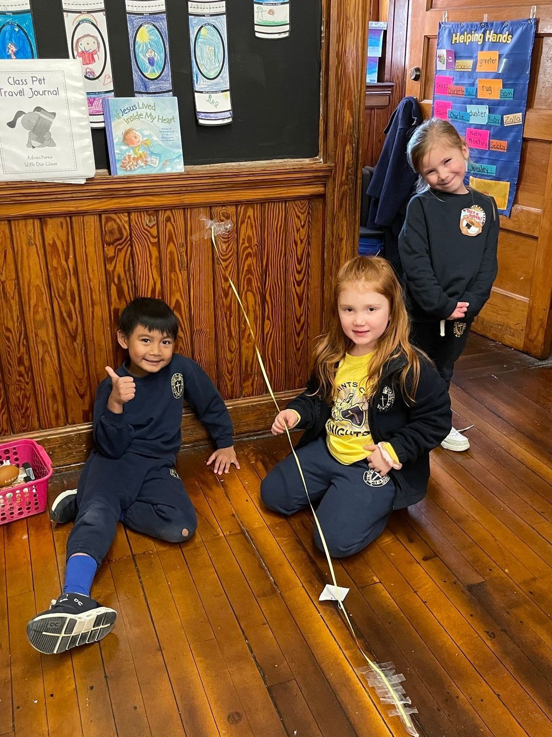 A boy and two girls are sitting on a wooden floor