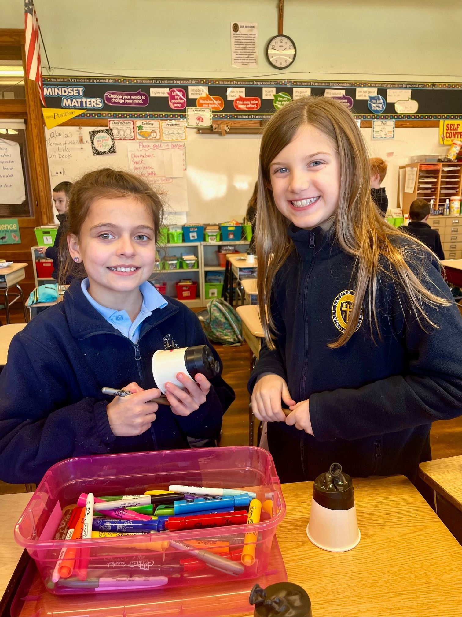 Two girls are standing next to each other in a classroom