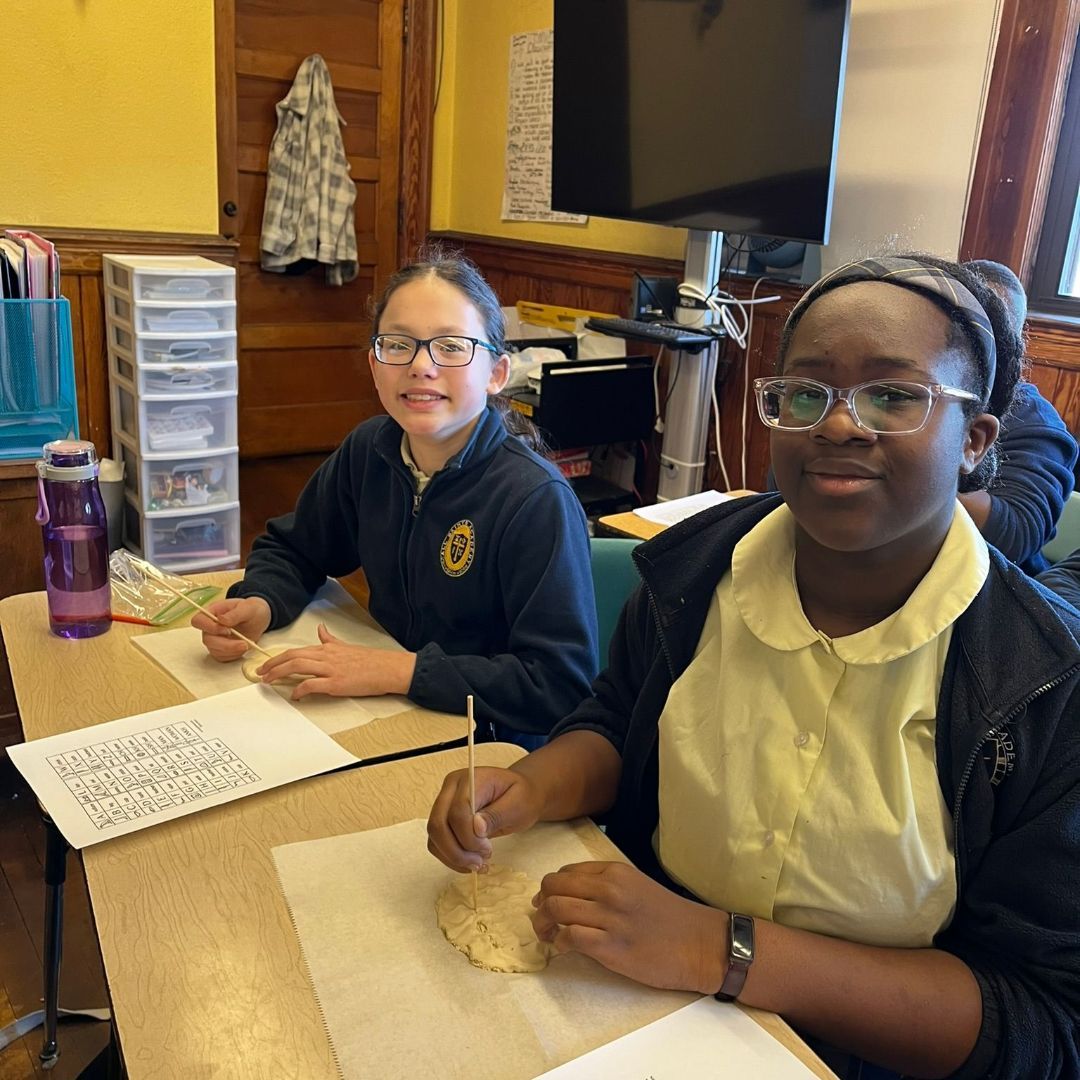 Two girls are sitting at a desk with a purple water bottle