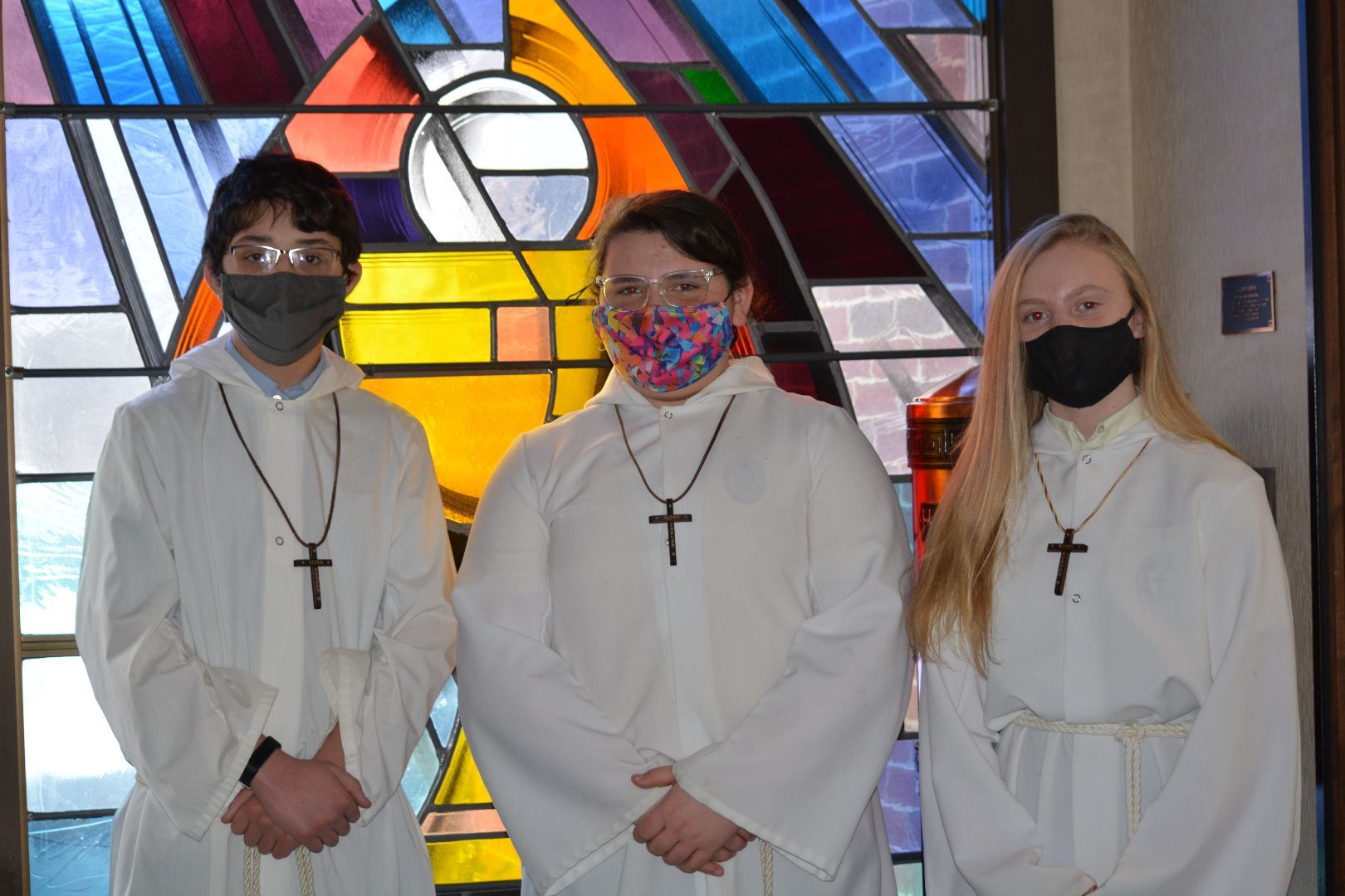 Three people wearing masks in front of a stained glass window