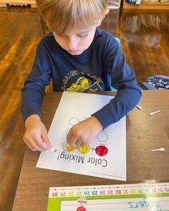 A young boy is sitting at a table playing with a color mixing activity.