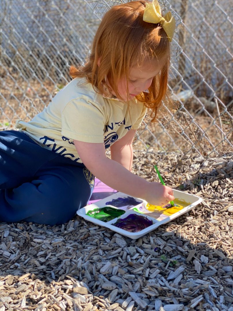 A little girl is kneeling on the ground painting on a tray.