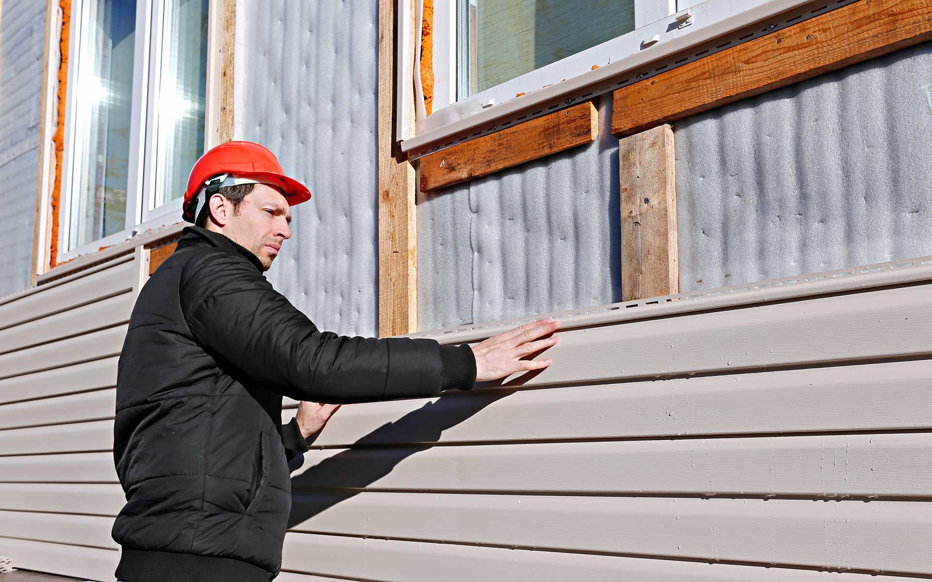 A worker installs panels beige siding on the facade 
