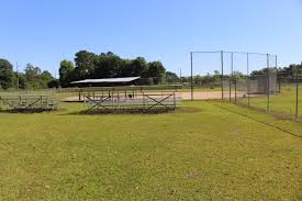 Baseball field with grass, a covered dugout, and a batting cage under a blue sky.